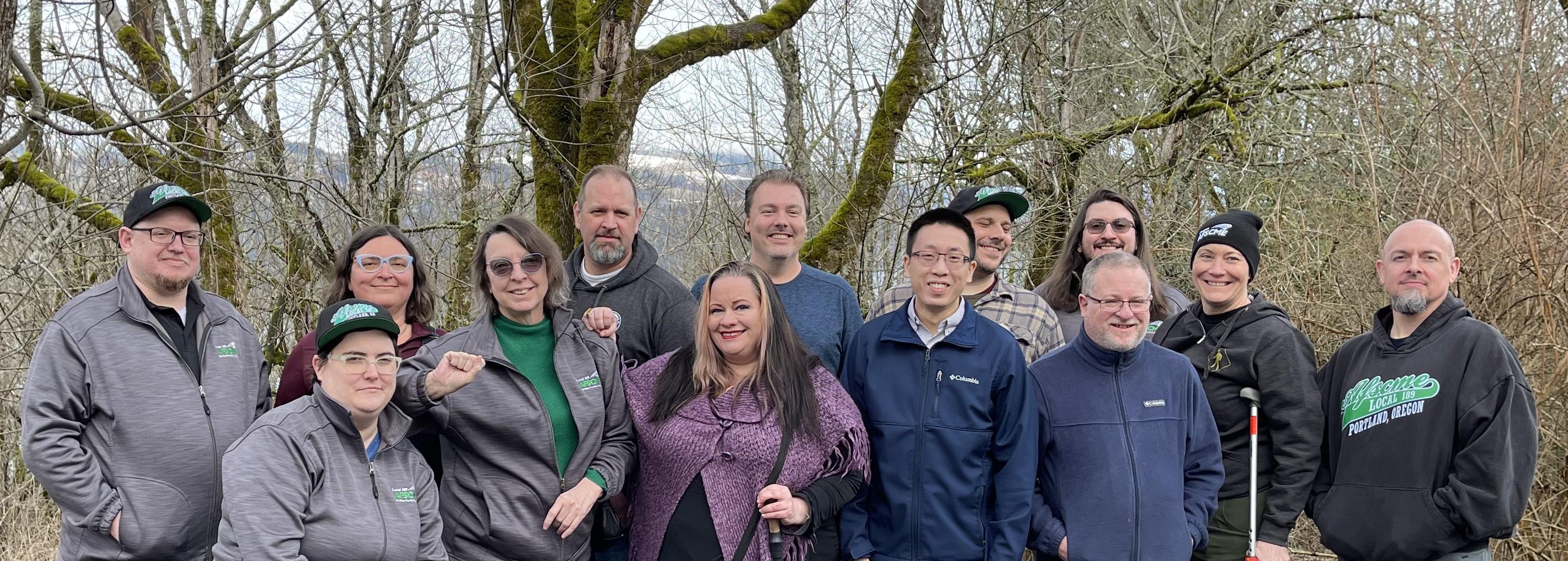 An image of several folks standing together against a scenic backdrop. Left to right: Dan, Chris F, Courtney, JoAnn, Rob, Amie, Chris R, Minh Dan, Alex, Jacob (foreground), Kelly, Tara, Chris P
